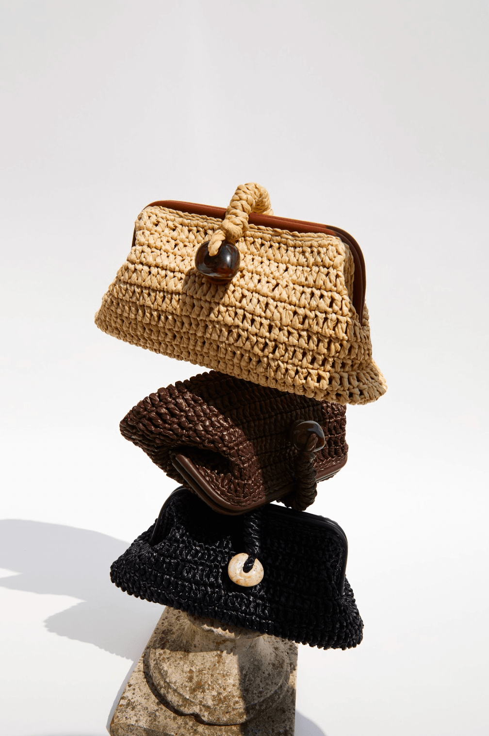 Stack of three stylish pouch bags in natural raffia, showcasing a rustic charm and elegant design.