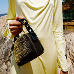 Model holding Catena Glitter Two Sided Bag, showcasing its sparkling exterior against a natural backdrop.
