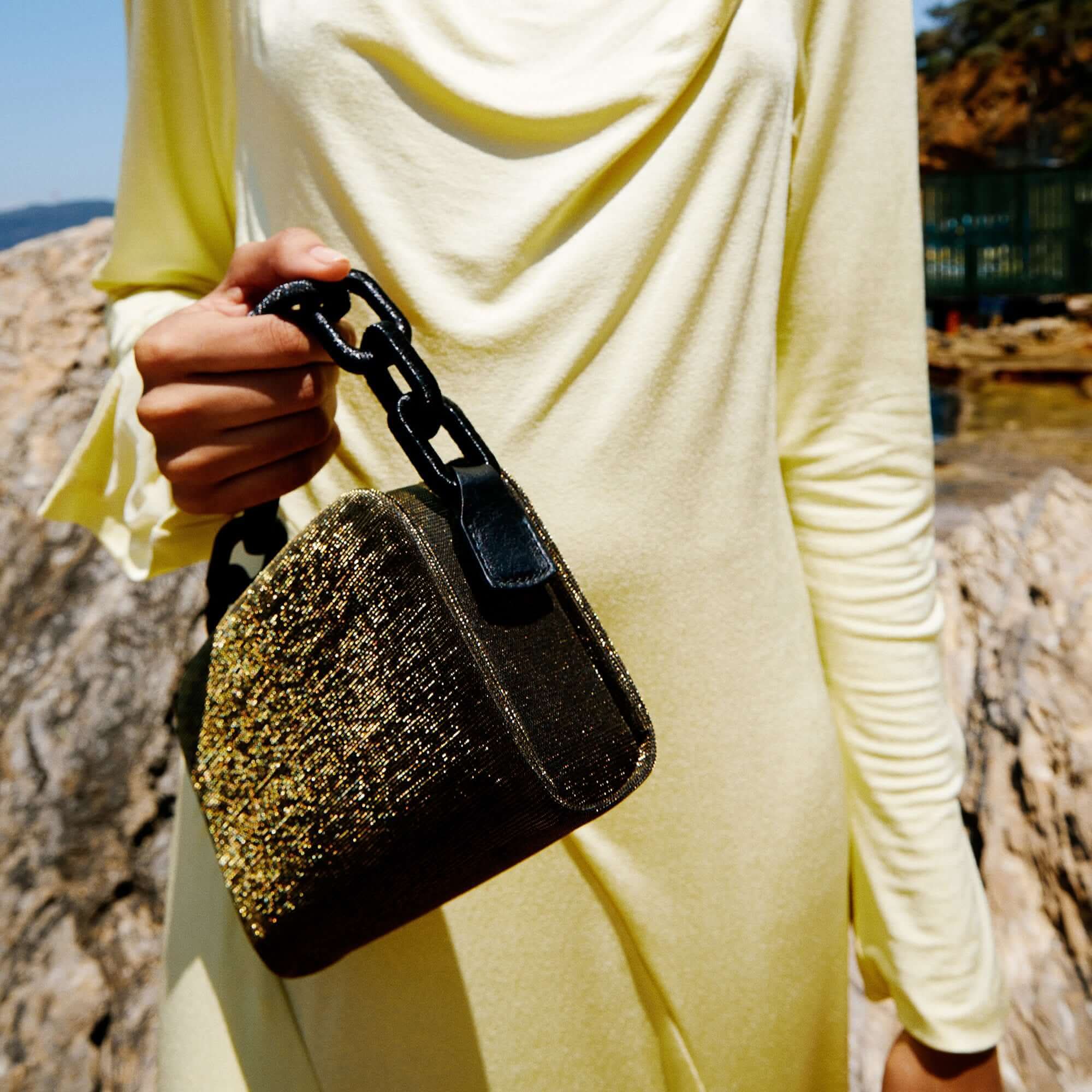 Model holding Catena Glitter Two Sided Bag, showcasing its sparkling exterior against a natural backdrop.
